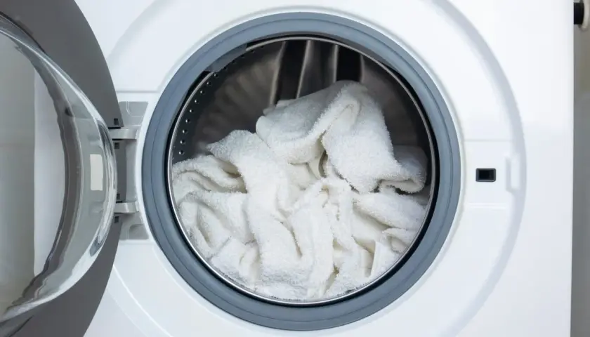 Tambour de machine à laver rempli de linge blanc prêt pour un lavage éclatant avec de l'eau de javel pour blanchir le linge en machine.