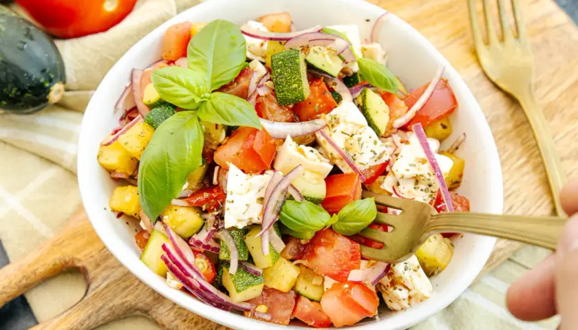 Frischer zucchini-salat mit feta, Tomaten, roten Zwiebeln und Basilikum, garniert mit Kräutern.