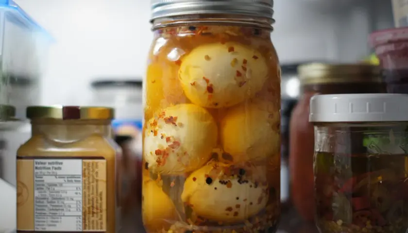 Un bocal rempli d'œufs au vinaigre, épicés et conservés dans un liquide ambré, se tient au premier plan.