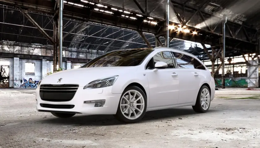 Biały Peugeot 508 SW na jasnych felgach, z widocznym rozmiarem opon, stoi w opuszczonej hali przemysłowej.