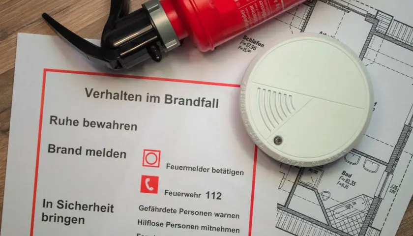 Brandschutz-Checkliste mit Feuerlöscher, Rauchmelder und Grundriss. Die Brandlast-Definition wird durch die gezeigten Elemente zur Brandverhütung verdeutlicht.