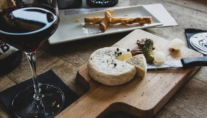 Verre de vin rouge avec un plateau de fromage, cornichons et noix. Un délice pour accompagner une dégustation de vin rouge avec charcuterie et fromage.