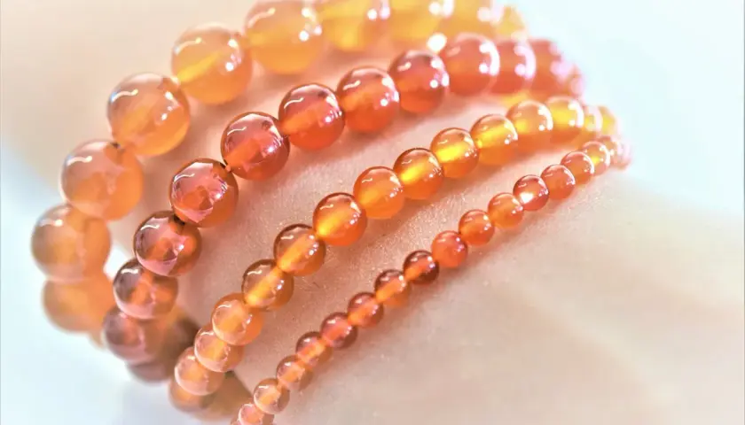 Armbänder aus leuchtenden, orange-roten Feuerachat-Kugeln in verschiedenen Größen, die wie ein warmer Sonnenuntergang auf der Haut liegen.