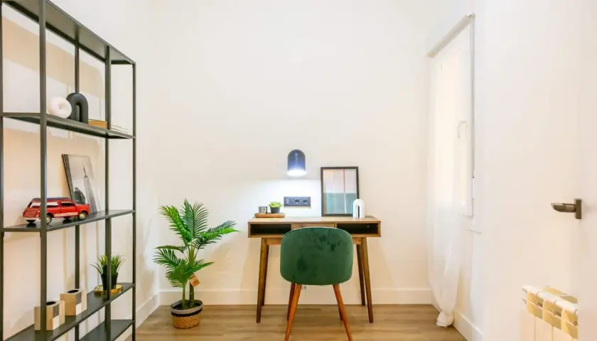 Escritorio de madera con silla verde, planta y estantería metálica. La luz de la lámpara es de 4000 K, creando un ambiente acogedor.