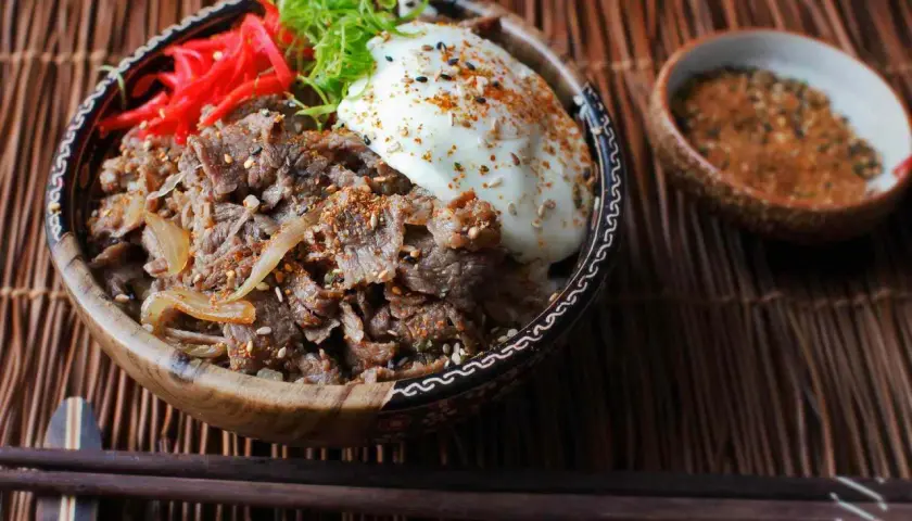 A delicious Yoshinoya beef bowl recipe, featuring tender beef, onions, a fried egg, pickled ginger, and green onions, ready to be enjoyed.