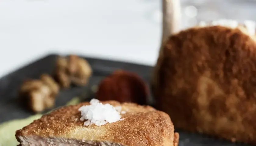 Ein knuspriges Kalbsschnitzel, italienisch zubereitet, mit feinen Beilagen auf einem dunklen Teller.