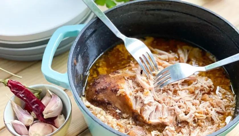 Szarpana wieprzowina w garnku, rozrywana widelcami, obok czosnek i papryczka chili.