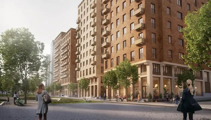 En modern stadsbild i Sverige med tegelbyggnader, balkonger och grönska. En kvinna med en väska går längs en stenlagd gata.