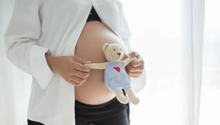 Brzuszek w białej koszuli, trzymający misia w pasiastym ubranku. Czas oczekiwania na dziecko, nadzieja na zdrowie, bez bólu reumatyzmu.