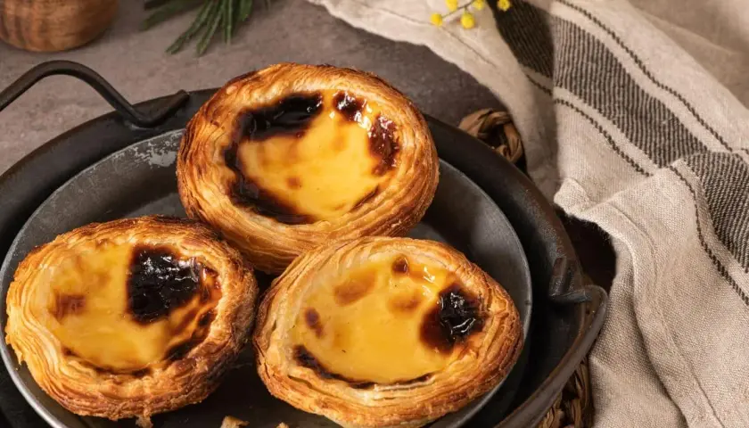 Trois délicieux flans portugais, dorés et caramélisés, sur un plateau en métal.