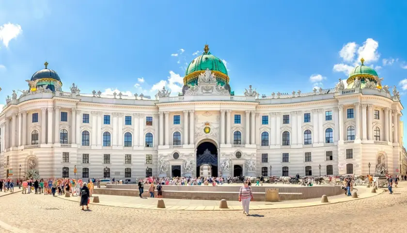 Majestatyczny pałac Sisi w Wiedniu, z zieloną kopułą i tłumem turystów na placu.