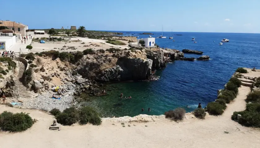 Gente nadando y tomando el sol en las calas de la isla Tabarca, con aguas cristalinas y barcos en el horizonte.