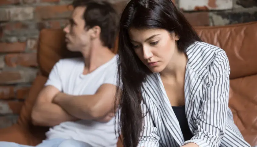 Una donna triste seduta su un divano, mentre suo marito non la desidera e le dà le spalle.