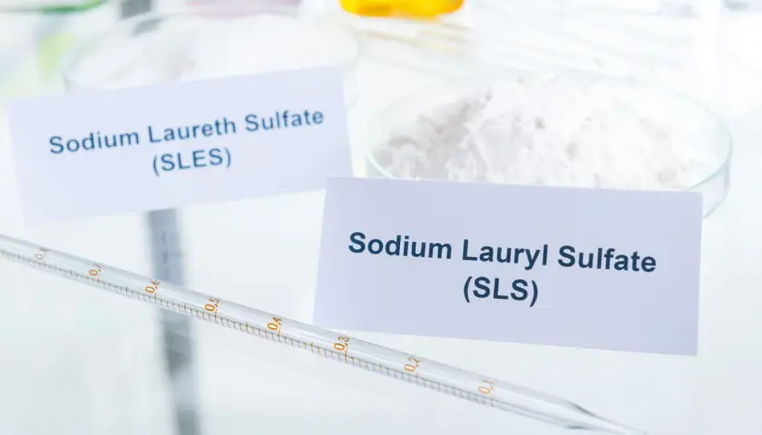 Białe proszki SLS i SLES w naczyniach laboratoryjnych, obok pipety.
