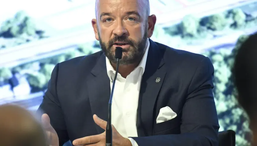 Jacek Sutryk z partnerem podczas konferencji prasowej. Mężczyzna w garniturze przemawia do mikrofonu.
