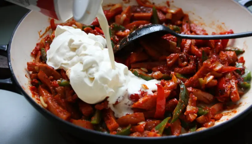 Gräddig korvgryta recept i pannan. Korv, paprika och lök blandas med en stor klick grädde.