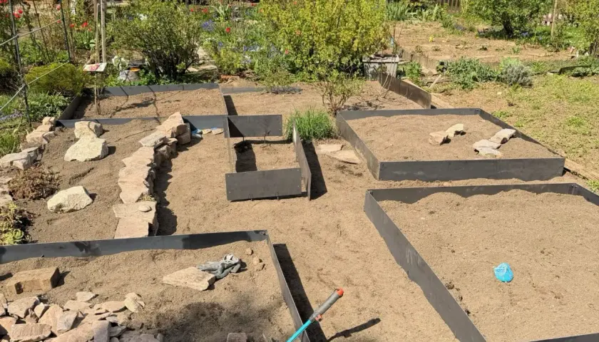 Gartenanlage mit Hochbeeten und naturnahen Gartenwegen aus Steinen. Werkzeuge liegen bereit.