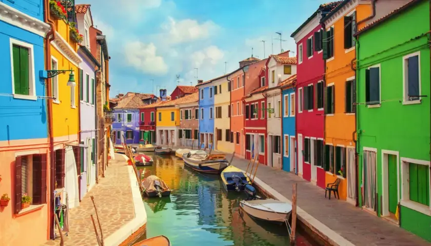 Colorate case affacciate su un canale a Burano, vicino a Murano. Barche ormeggiate riflettono i colori vivaci.
