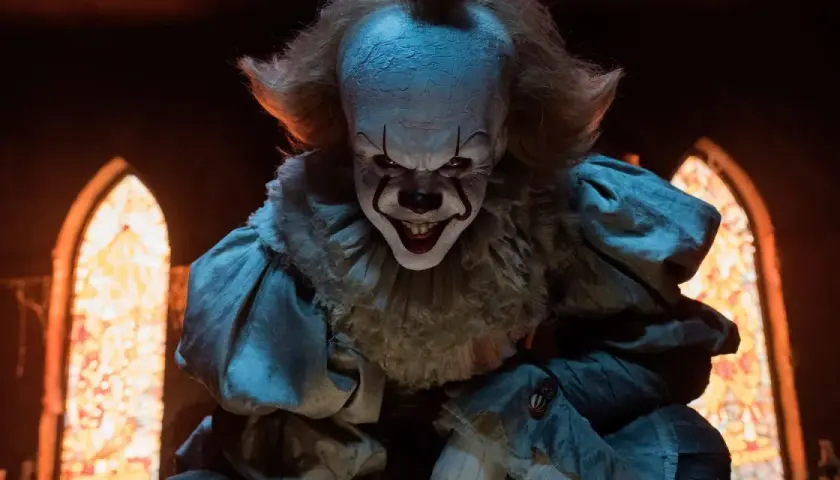 Gripsou le clown dansant, au sourire terrifiant, se tient dans une église sombre, ses yeux brillants fixant l'objectif.