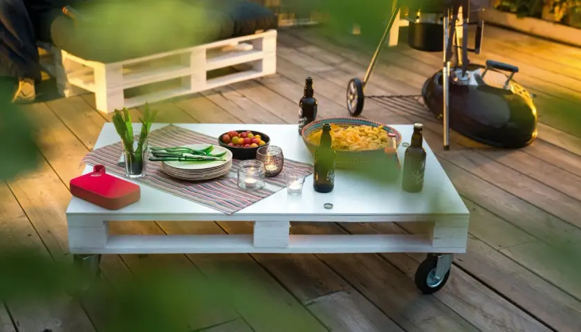 Tavolo fai da te con snack, bevande e candele su un deck di legno, pronto per una grigliata.