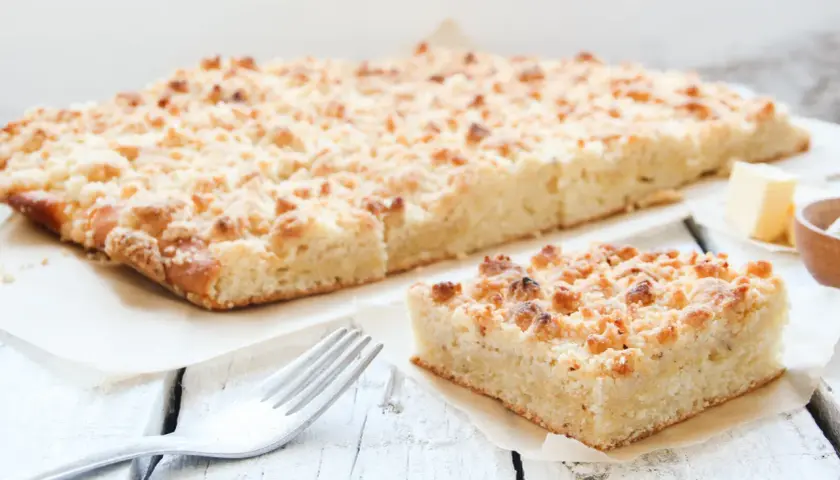 Ein Stück saftiger low carb streusel Kuchen mit Butter und einer Gabel auf einem Holztisch.