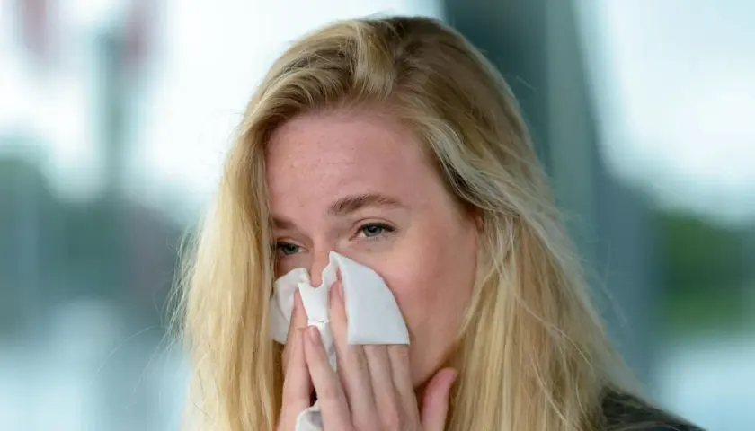 Blondynka z piegami chusteczką wyciera nos. Może to być objaw przeziębienia, alergii lub po prostu emocji. Jovesto.
