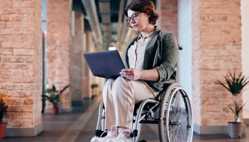 Kobieta na wózku inwalidzkim pracuje na laptopie. Czy lekarz rodzinny może wystawić zlecenie na wózek inwalidzki?