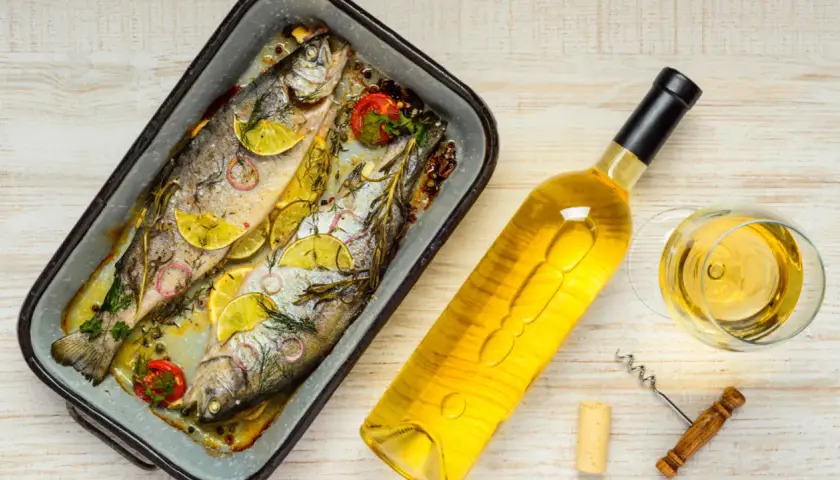 Zwei gebackene Forellen mit Zitrone und Kräutern, daneben eine Flasche Weißwein und ein Glas. Perfekt, welcher Wein zu Lachs passt, ist hier schon fast klar.