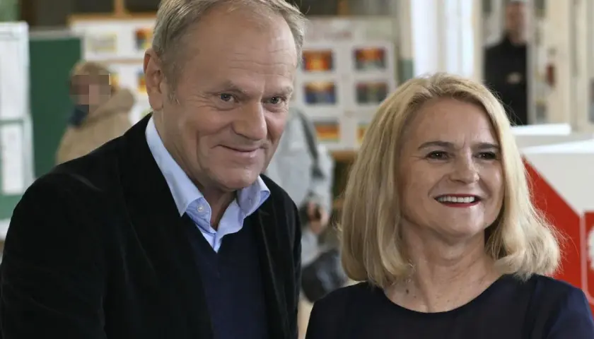Donald Tusk z żoną, uśmiechnięci, w tle wyborcze plakaty.