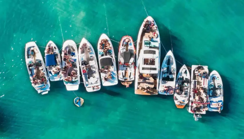 Grupa łodzi cumuje blisko siebie na turkusowej wodzie, tworząc wrażenie wodnego festiwalu. To idealny prom majorka ibiza dla miłośników słońca i zabawy na morzu.