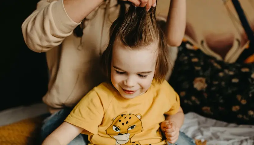 Mama delikatnie rozczesuje kołtuny u dziecka, które uśmiecha się, patrząc w dół.