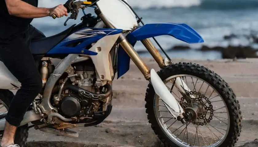 Persona sentada en una moto de cross azul y blanca en la arena, con el mar al fondo. ¿Cuánto paga un desguace por una moto?
