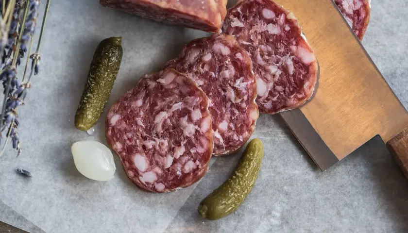 Plasterki salami z widocznym tłuszczem, ogórki konserwowe i cebulka. Salami jest z mięsa wieprzowego i wołowego.
