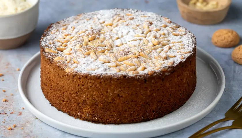 Torta rustica con farina di mandorle, cosparsa di zucchero a velo e pinoli tostati. Un dolce invitante, perfetto per ogni occasione.