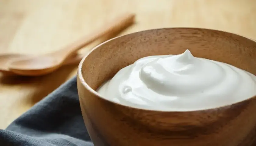 Una ciotola di legno contiene una soffice crema al latte, pronta per essere gustata. Due cucchiai di legno sono sullo sfondo.