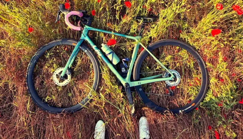 Zielony rower leżący na łące pełnej maków, z widocznymi butami rowerowymi.