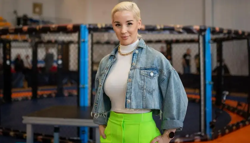 Kobieta w dżinsowej kurtce i neonowych spodniach stoi przed klatką MMA. Ile lat ma Aniela Bogusz?