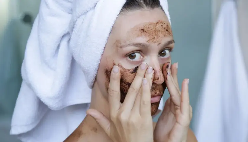 Kobieta z ręcznikiem na głowie nakłada na twarz domowy peeling złuszczający do twarzy.