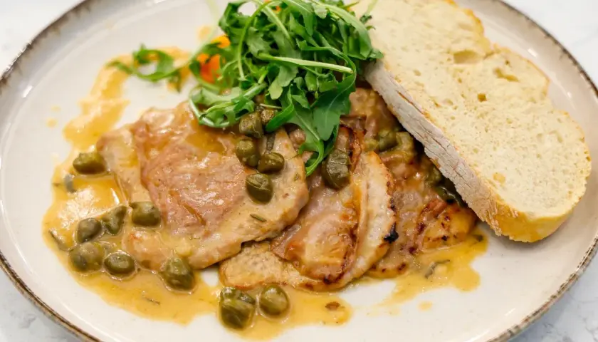 Pyszne saltimbocca alla romana z cielęciną, szynką, szałwią i kaparami w sosie, podane z rukolą i chlebem.