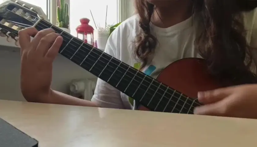 Osoba gra na gitarze klasycznej, ćwicząc znane utwory na gitarę klasyczną.