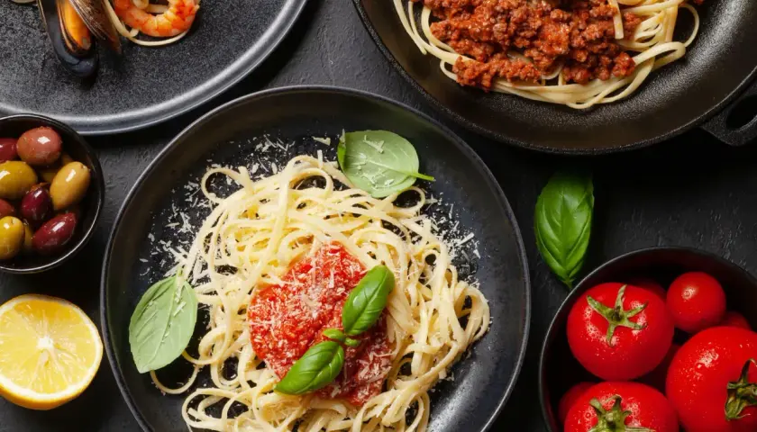 Pyszne spaghetti z sosem pomidorowym i bazylią, posypane czymś, co świetnie sprawdzi się co zamiast parmezanu. Obok talerz z owocami morza i mięsem mielonym.