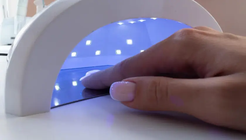 Dłoń z paznokciami w lampie UV. Zastanawiasz się, jaka moc lampy do paznokci będzie najlepsza?