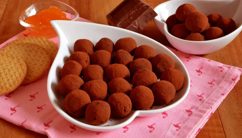 Bon bon cioccolato e panna anni '80, un dolce ricordo. Praline al cacao su un piatto bianco, con biscotti e marmellata d'arancia.