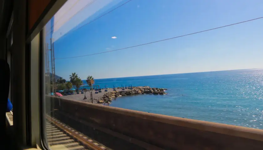 Tågluffa i Italien längs kusten, med blått hav och palmer som susar förbi fönstret.