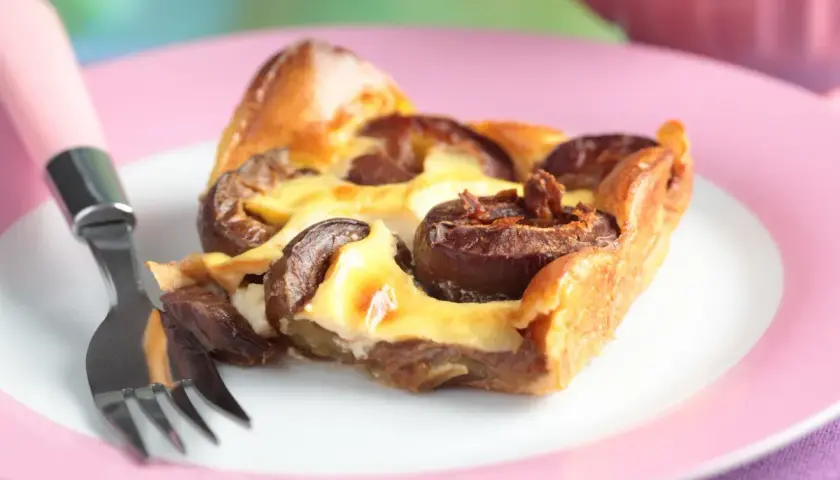 Tranche de clafoutis aux prunes moelleux sur une assiette rose avec une fourchette.