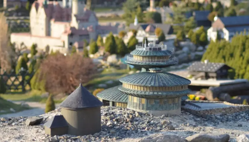 Miniaturowe budowle, w tym okrągły budynek z kopułą i wielopoziomowa konstrukcja, tworzą krajobraz jednego z parków miniatur w Polsce.