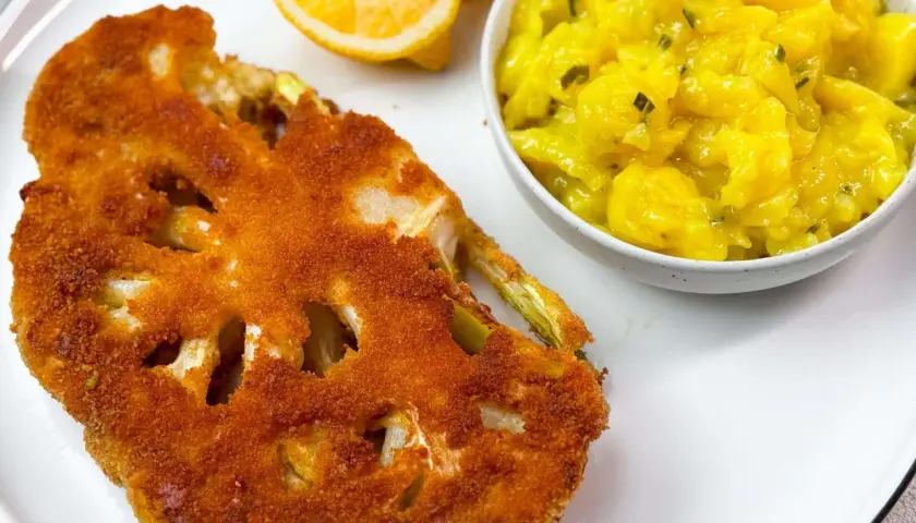 Knuspriges Blumenkohl-Schnitzel mit Kartoffelsalat und Zitronenspalten auf einem weißen Teller.