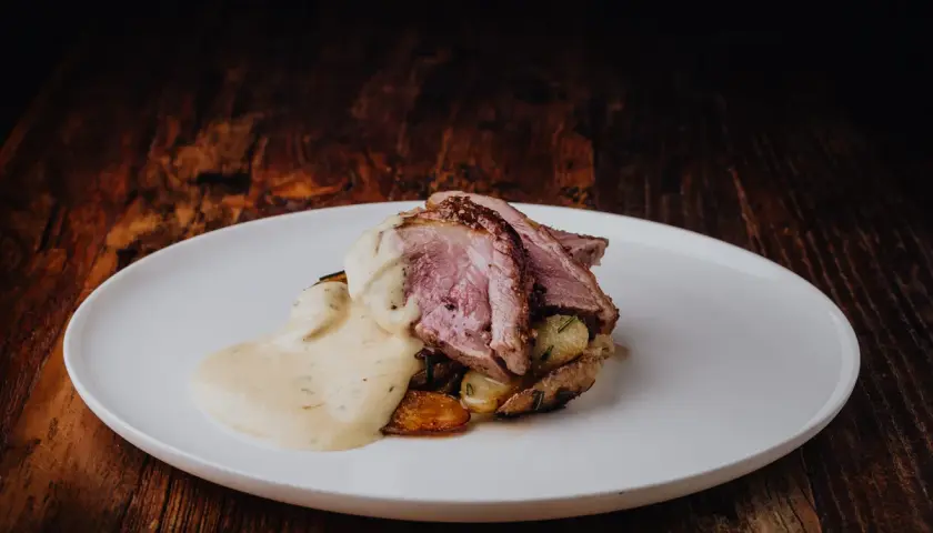 Tranches de gigot d'agneau au four, nappées d'une sauce crémeuse, servies sur des pommes de terre rôties. Un délice visuel et gustatif.