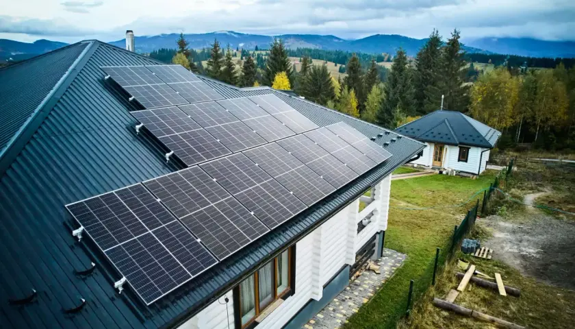 Häuser mit Solarmodulen auf dem Dach, bereit, Solarstrom zu verkaufen. Im Hintergrund bewaldete Hügel.