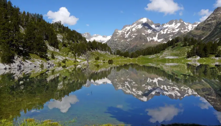 Espejo de agua en los valles de Huesca, reflejando montañas nevadas y un cielo azul con nubes.